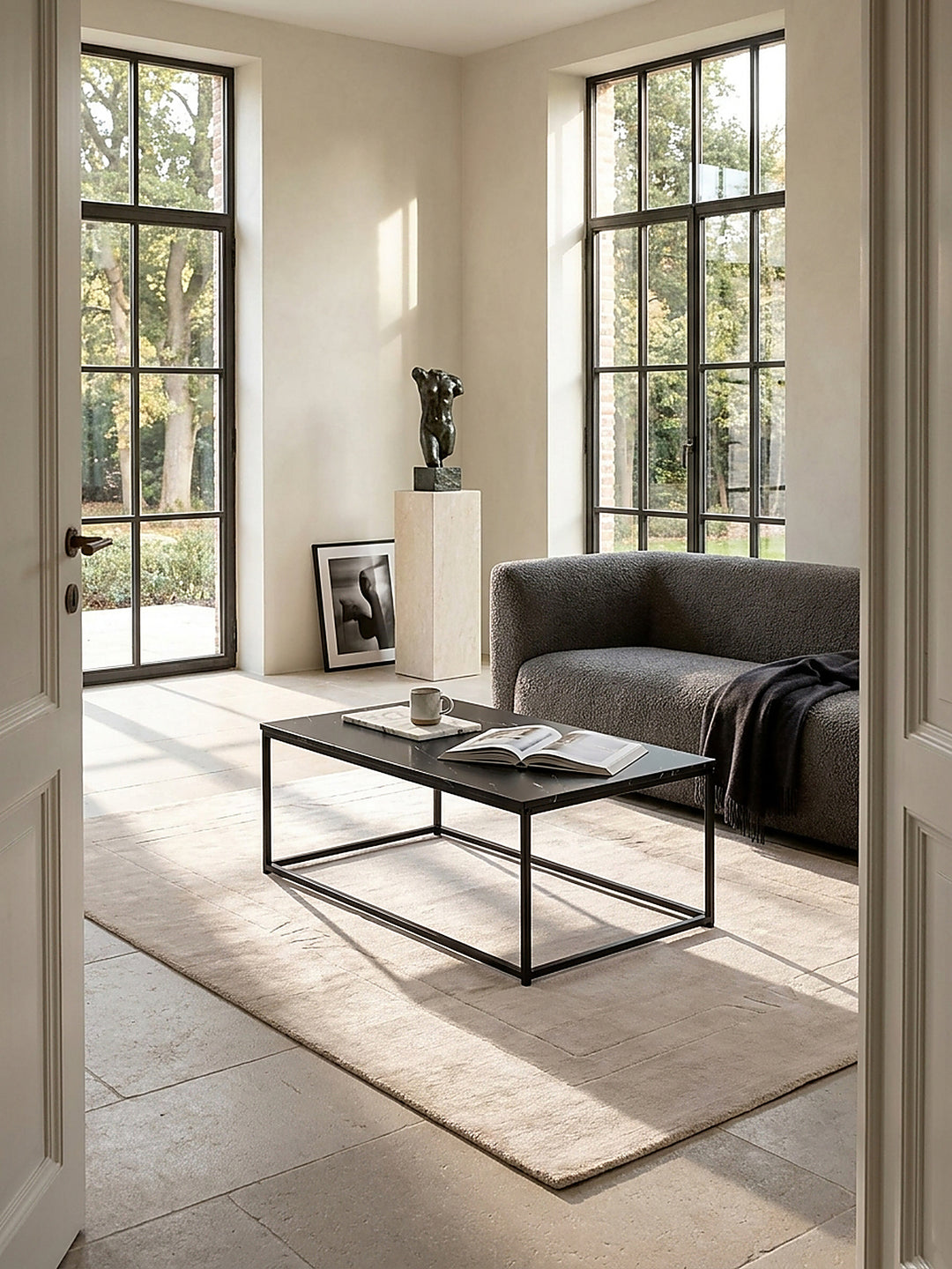 Rechteckiger Couchtisch mit dunkler Marmor-Optik und filigranem Metallgestell im puristischen Wohnzimmer, elegant inszeniert auf geschliffenem Kalksteinboden vor einer hellen Fensterfront_