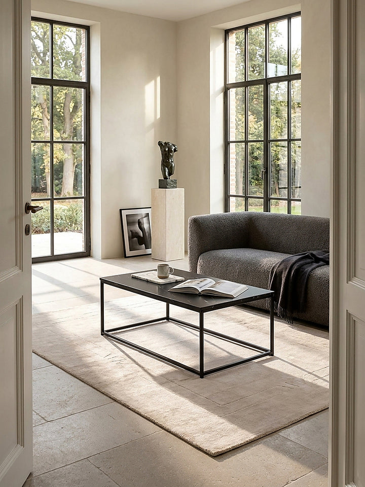 Rechteckiger Couchtisch mit dunkler Marmor-Optik und filigranem Metallgestell im puristischen Wohnzimmer, elegant inszeniert auf geschliffenem Kalksteinboden vor einer hellen Fensterfront_