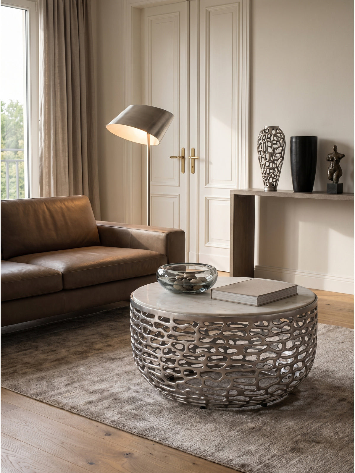Couchtisch Silber Weiß kombiniert mit einem dunkelgrauen Sessel und einer skulpturalen Stehlampe im zeitgenössischen Wohnbereich_