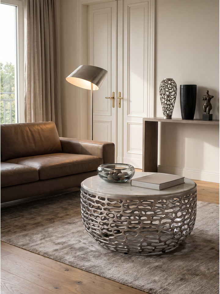 Couchtisch Silber Weiß kombiniert mit einem dunkelgrauen Sessel und einer skulpturalen Stehlampe im zeitgenössischen Wohnbereich_