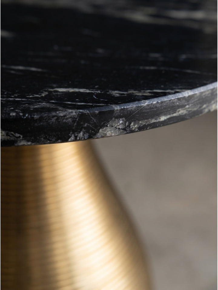 Detailaufnahme der glatten schwarzen Marmorplatte und der feinen Rillenstruktur des goldenen Aluminiumfußes im warmen Sonnenlicht_