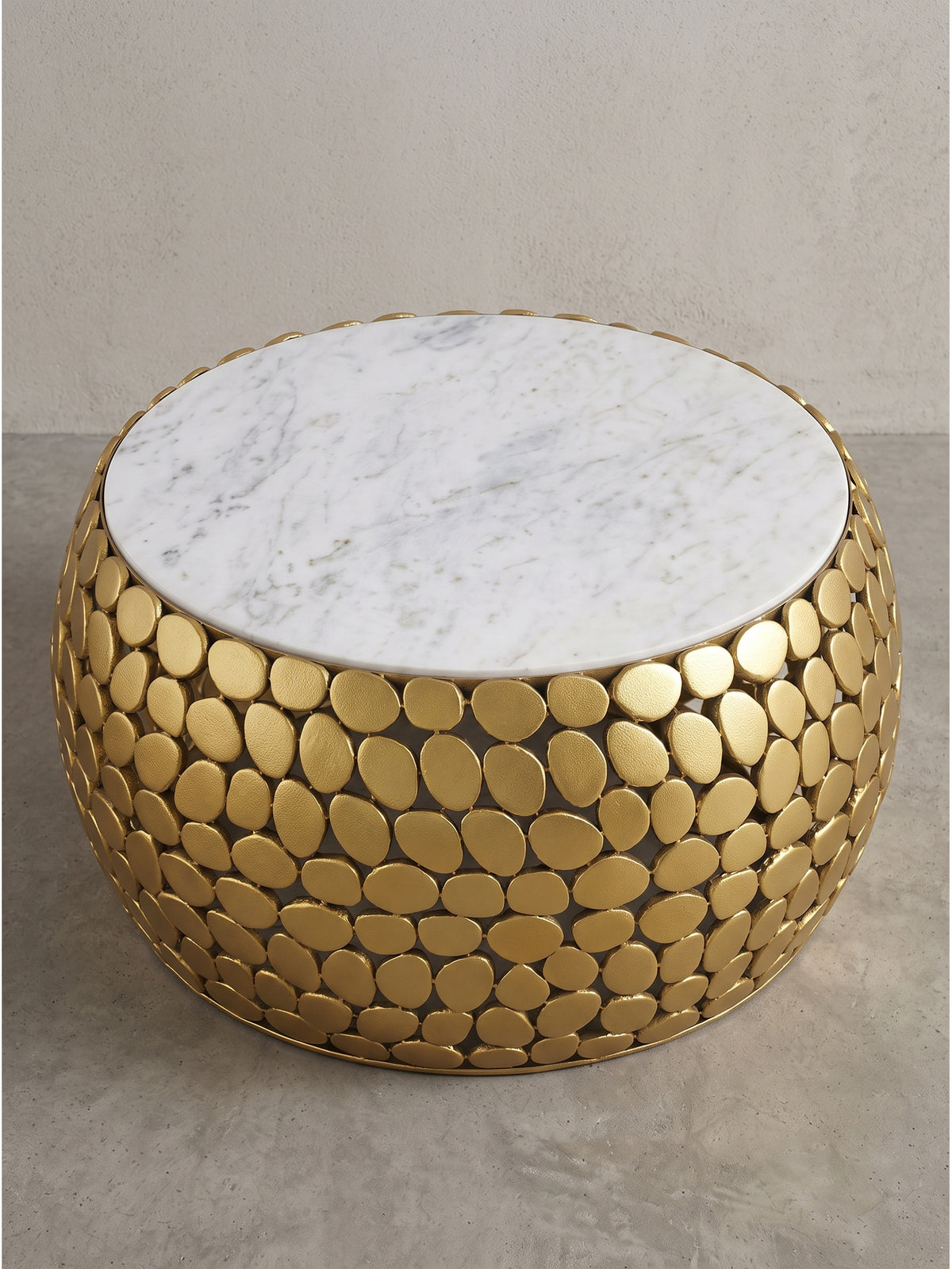Eleganter Sofatisch mit durchbrochenem, goldfarbenem Metallkorpus und massiver Steinplatte in halbseitlicher Perspektive auf weißem Grund._