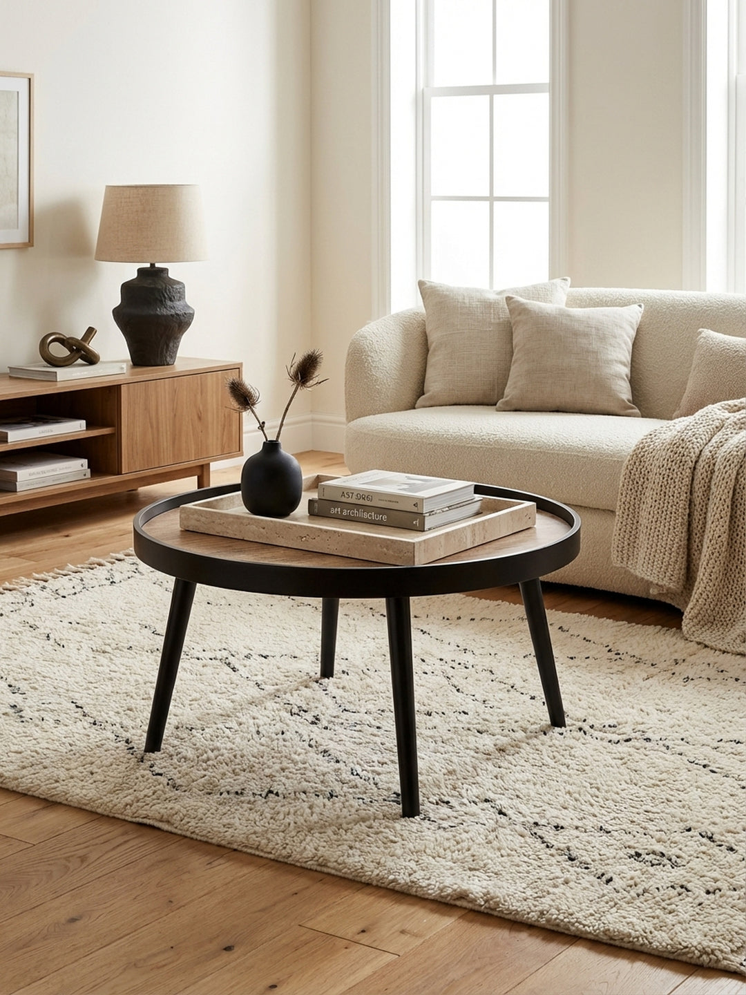 Eleganter runder Couchtisch mit schwarzem Gestell und Holzplatte in einem modern eingerichteten Wohnzimmer mit cremefarbenem Teppich und Sofa._