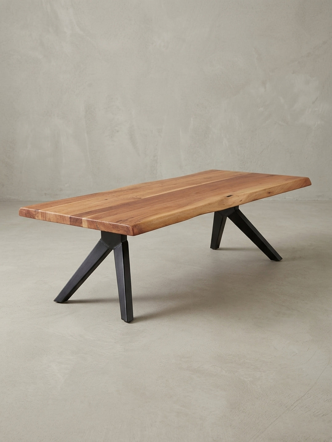 Dreiviertelansicht des rechteckigen Wohnzimmertisches, die das Zusammenspiel der massiven Holzplatte und der geometrischen, pulverbeschichteten Edelstahlbeine zeigt._