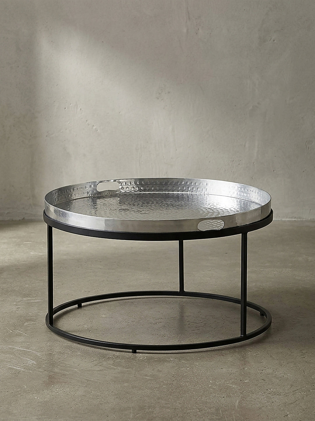 Freigestellter runder Couchtisch mit silberner Aluminiumplatte und schwarzem Metallrahmen frontal vor weißem Hintergrund._