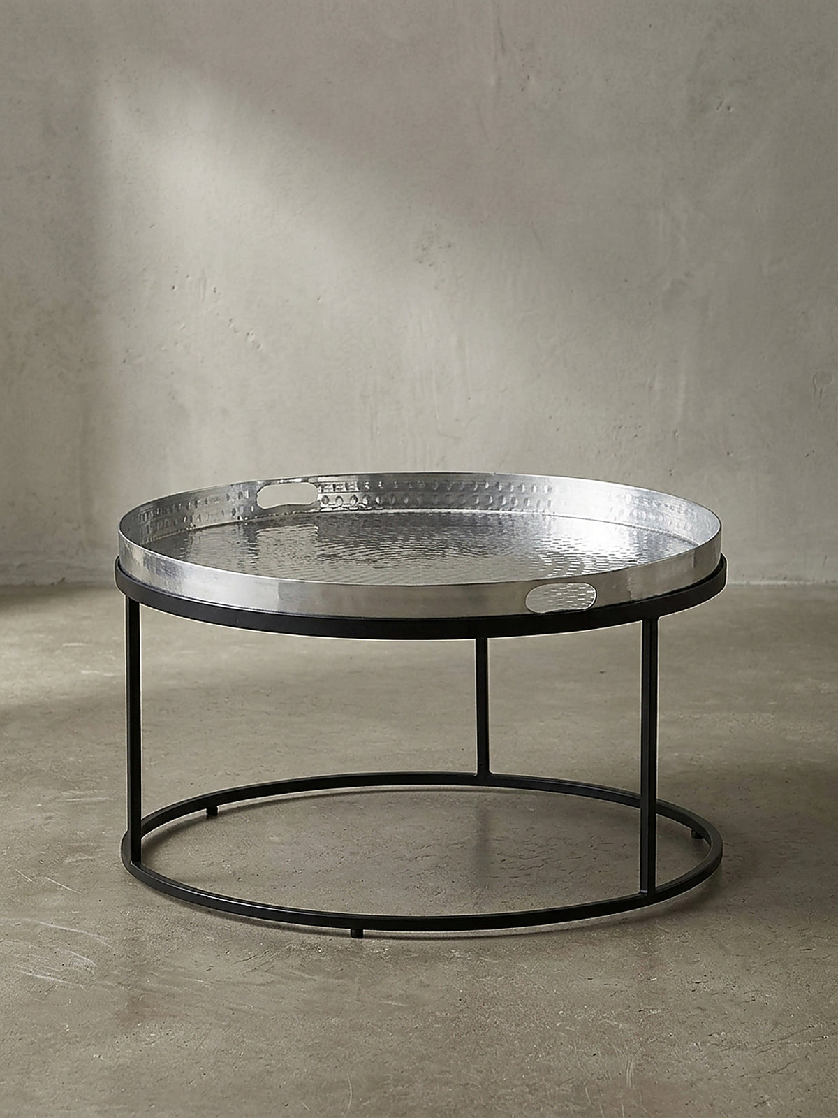 Freigestellter runder Couchtisch mit silberner Aluminiumplatte und schwarzem Metallrahmen frontal vor weißem Hintergrund.