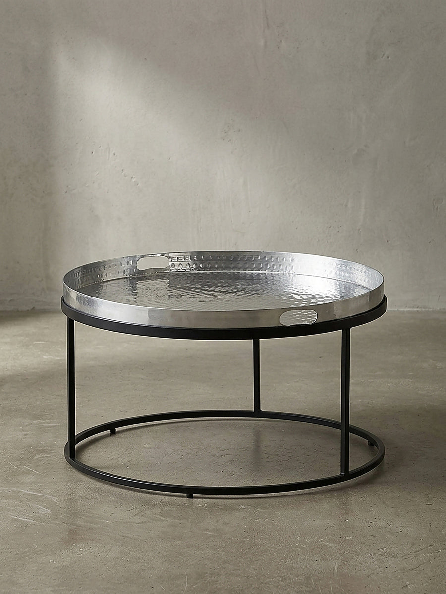 Freigestellter runder Couchtisch mit silberner Aluminiumplatte und schwarzem Metallrahmen frontal vor weißem Hintergrund._