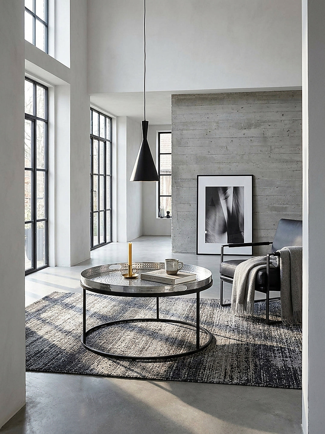Runder Couchtisch aus gehämmertem Aluminium in Silber und schwarzem Eisengestell 62x62x36 cm im modernen Wohnzimmer auf poliertem Betonboden._