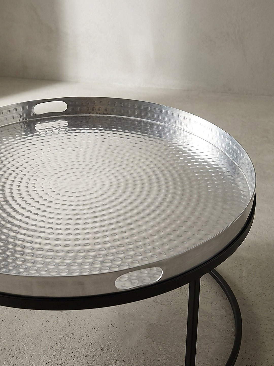 Gesamtdesign des minimalistischen Wohnzimmertisches mit gehämmertem Silbertablett und mattschwarzen Beinen in Studiobeleuchtung._