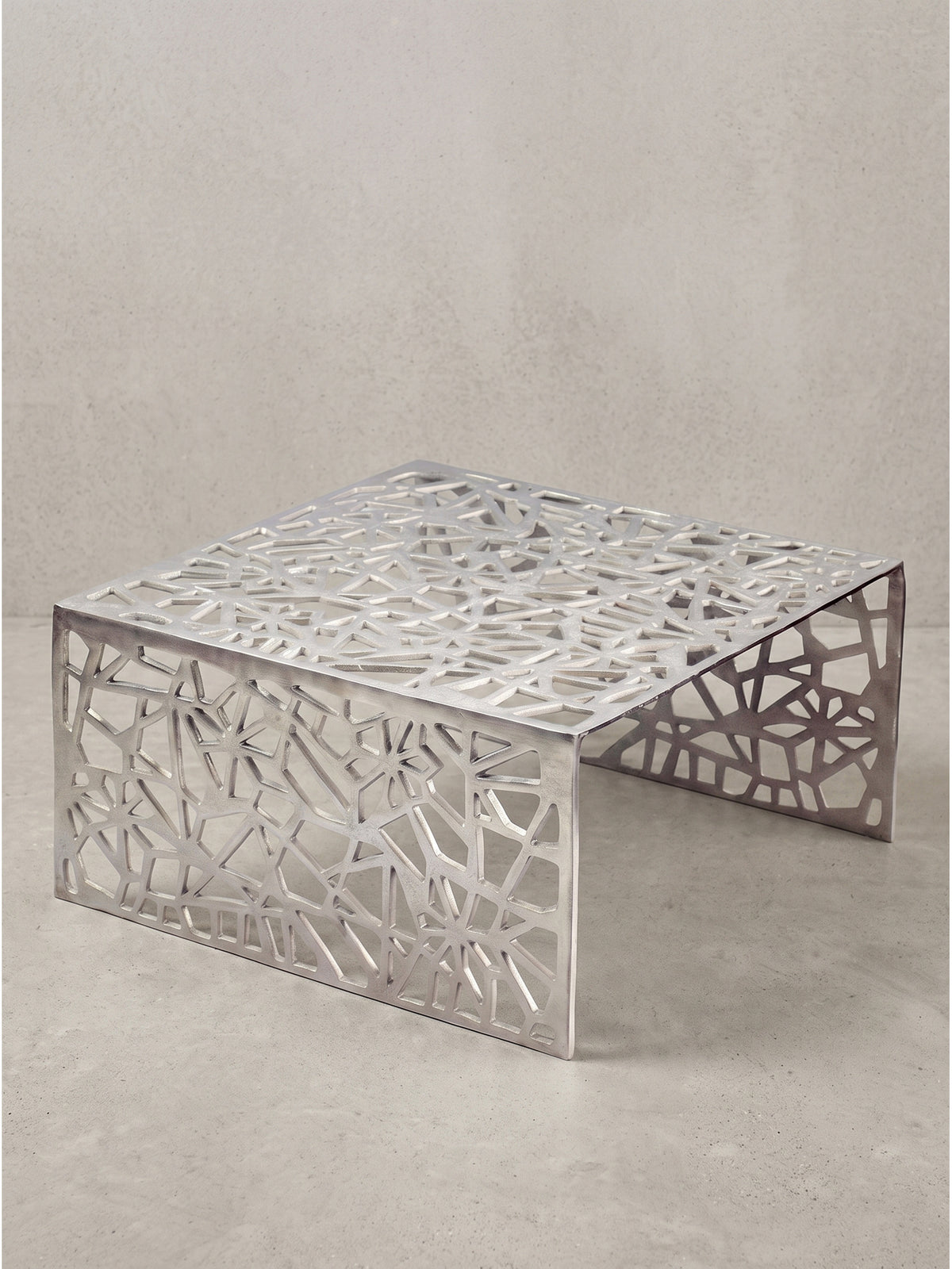 Nahaufnahme der kühlen Materialbeschaffenheit des Couchtisches aus reinem Aluminium mit präzisen, geometrischen Aussparungen_