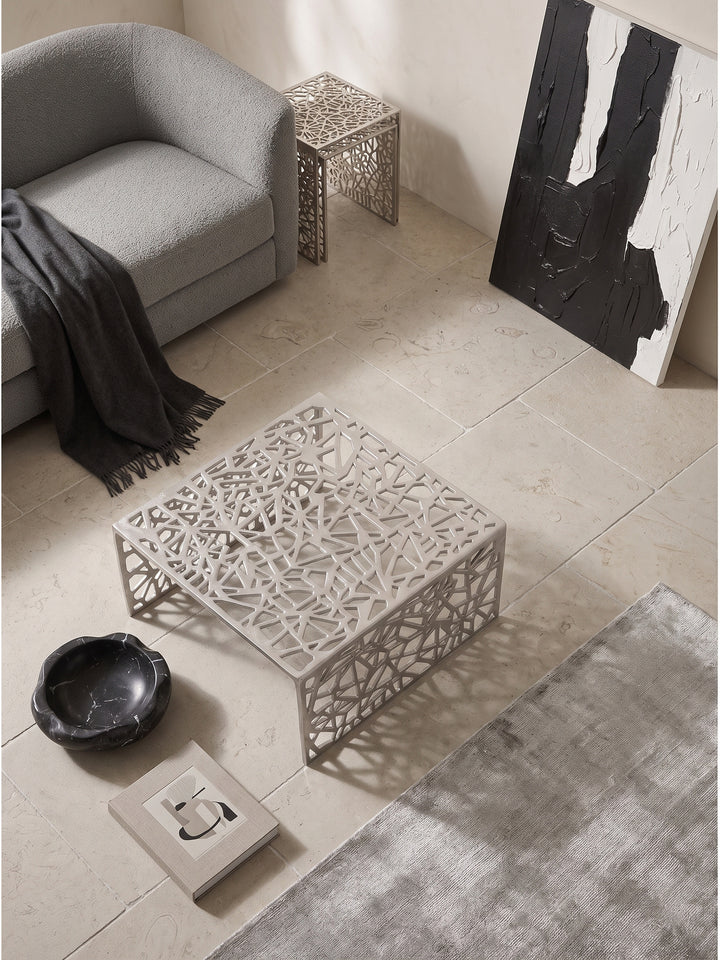 Draufsicht auf den 60x60 cm großen Sofatisch aus Metall neben einem grauen Bouclé-Sofa auf hellem Kalksteinboden_
