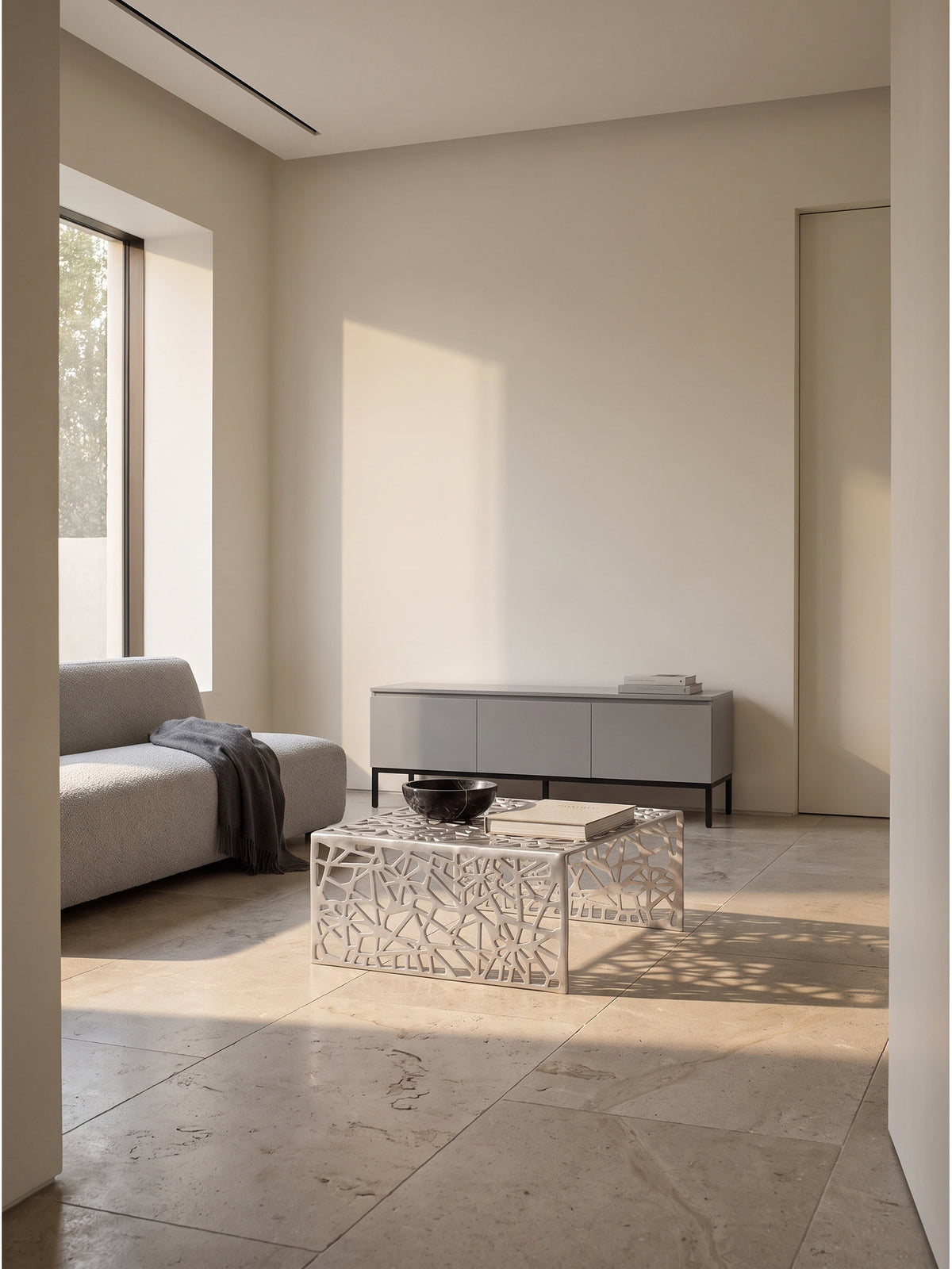 Quadratischer Couchtisch aus silbernem Aluminium mit netzartigem Muster im minimalistischen Wohnzimmer vor heller Putzwand_