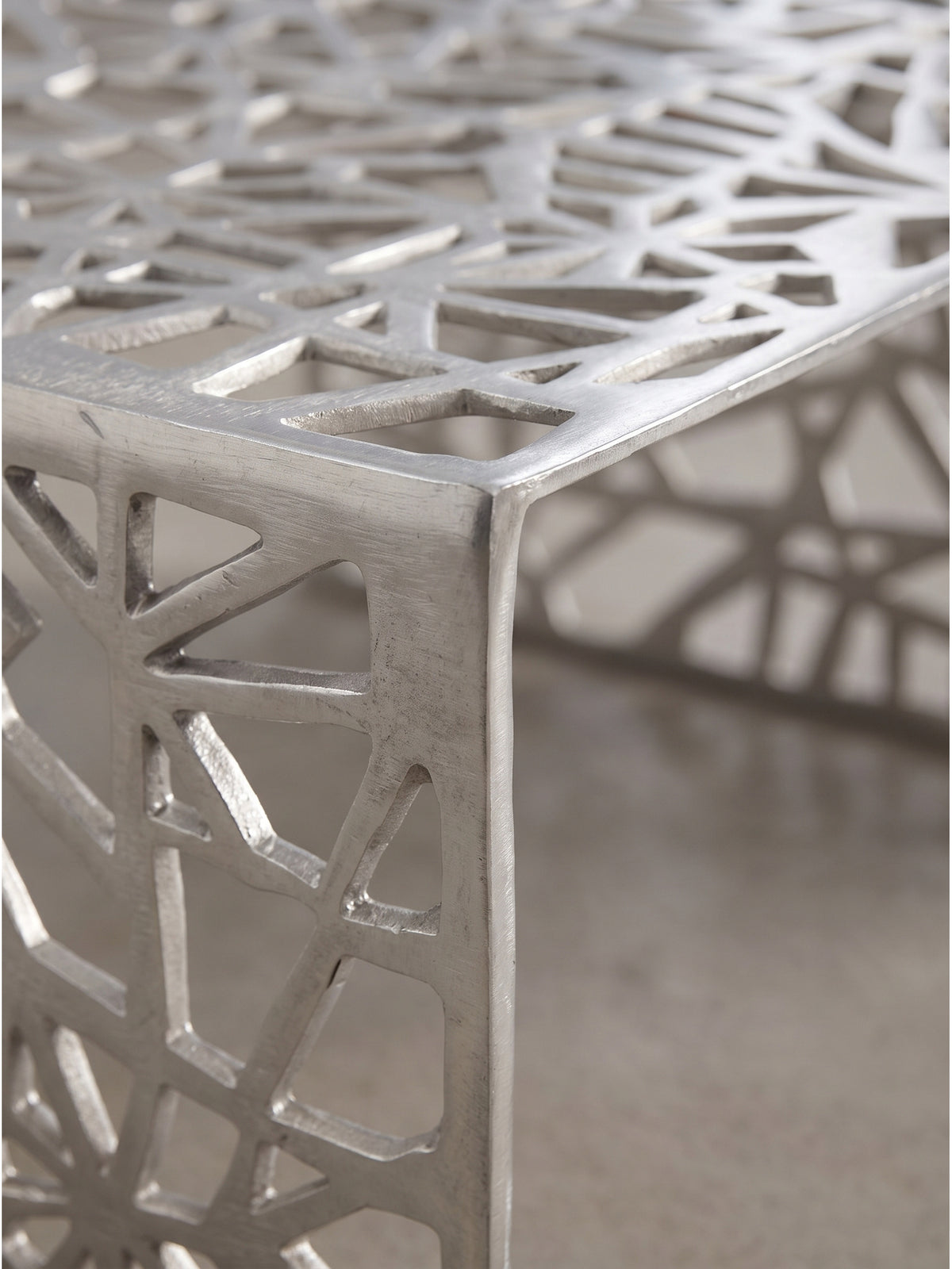Detailaufnahme des organischen Durchbruchmusters am silbernen Aluminiumtisch mit architektonischer Netzstruktur_
