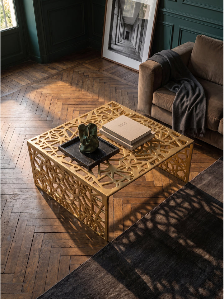 Blick von oben auf den flachen Loungetisch aus Metall neben einem taupefarbenen Samtsofa auf anthrazitfarbenem Seidenteppich._