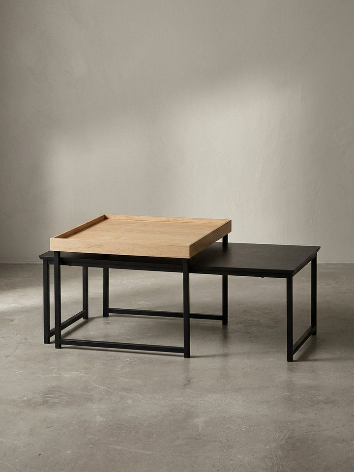 Moderner Satztisch bestehend aus zwei flexiblen Elementen mit schwarzem Metallgestell und unterschiedlich hohen Tischplatten in Natureiche und Schwarz freigestellt._