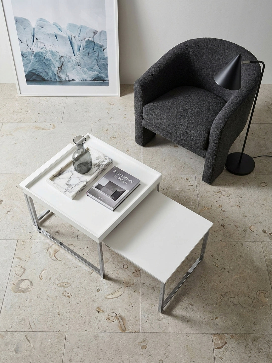 Draufsicht auf das eckige Beistelltisch Set in Weiß und Silber neben einem anthrazitfarbenen Sofa und architektonischen Bildbänden._
