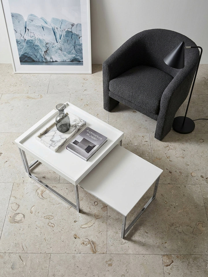 Draufsicht auf das eckige Beistelltisch Set in Weiß und Silber neben einem anthrazitfarbenen Sofa und architektonischen Bildbänden._