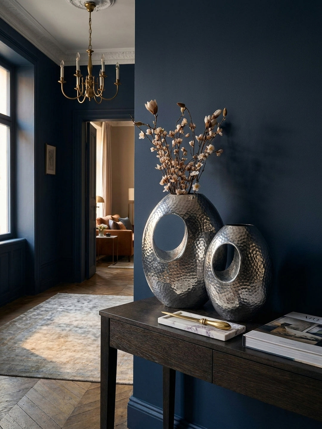 Detailaufnahme der gehämmerten Hammerschlag-Oberfläche einer silbernen Design-Vase, die das Licht in feinen Facetten reflektiert._