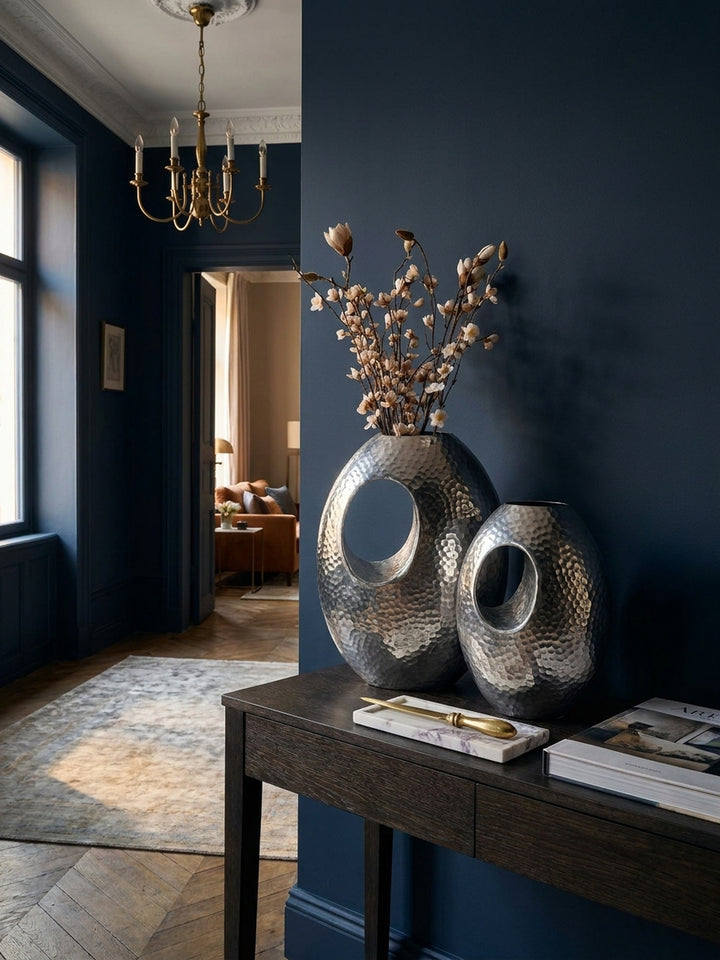 Detailaufnahme der gehämmerten Hammerschlag-Oberfläche einer silbernen Design-Vase, die das Licht in feinen Facetten reflektiert._