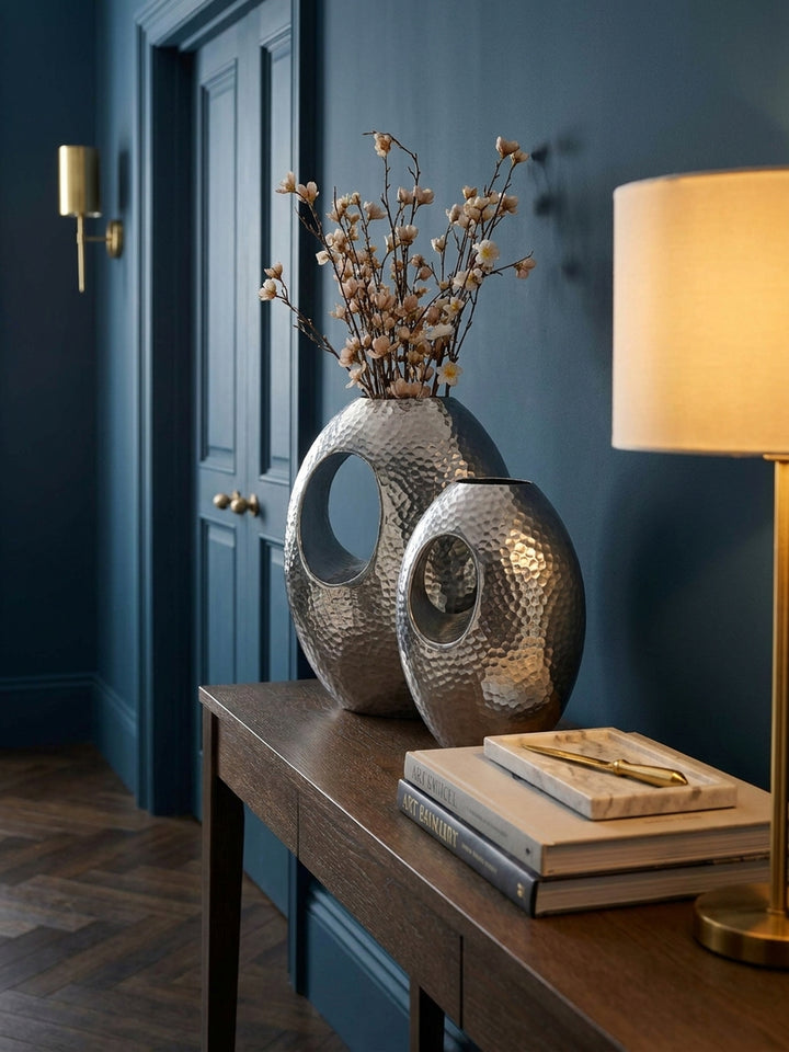 Stilvolles Deko-Arrangement mit einer modernen Blumenvase aus Aluminium neben einem Stapel Bildbände auf einem Sideboard._