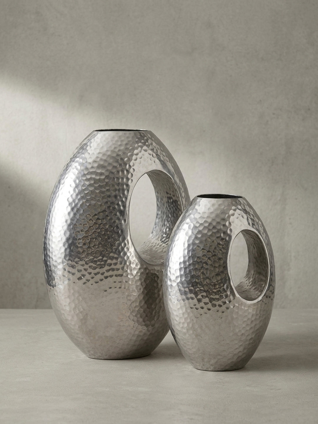 Skulpturale Blumenvase aus massivem Aluminium in Silber, handgefertigt mit charakteristischer Öffnung, aus einer 3/4-Perspektive gezeigt._