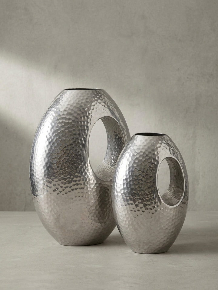 Skulpturale Blumenvase aus massivem Aluminium in Silber, handgefertigt mit charakteristischer Öffnung, aus einer 3/4-Perspektive gezeigt._