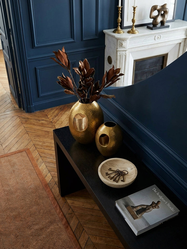 Draufsicht auf ein modernes Arrangement mit der handgefertigten Hammerschlag-Vase in Gold, platziert auf einem Beistelltisch neben einem Kunstbuch und einer Lampe._