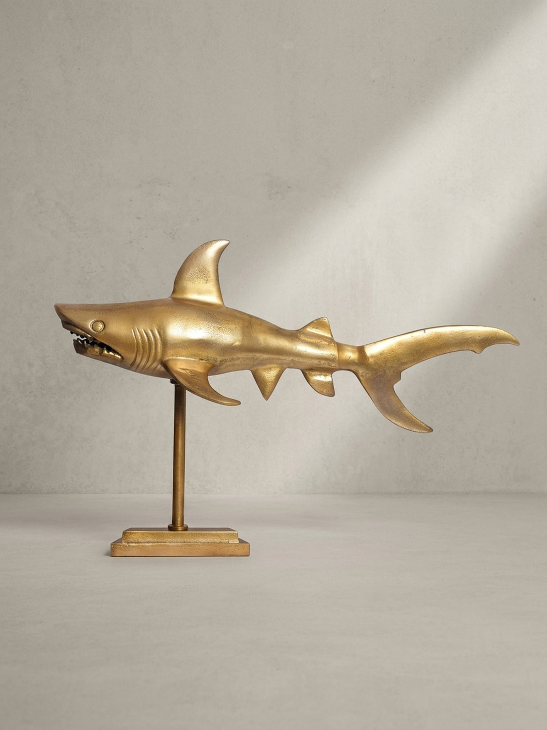 Dreiviertelansicht der Design-Dekofigur Hai aus mattgoldenem Aluminium, die die detaillierte Ausarbeitung der Flossen und des Kopfes hervorhebt._