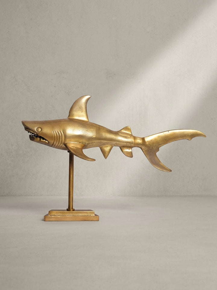 Dreiviertelansicht der Design-Dekofigur Hai aus mattgoldenem Aluminium, die die detaillierte Ausarbeitung der Flossen und des Kopfes hervorhebt._