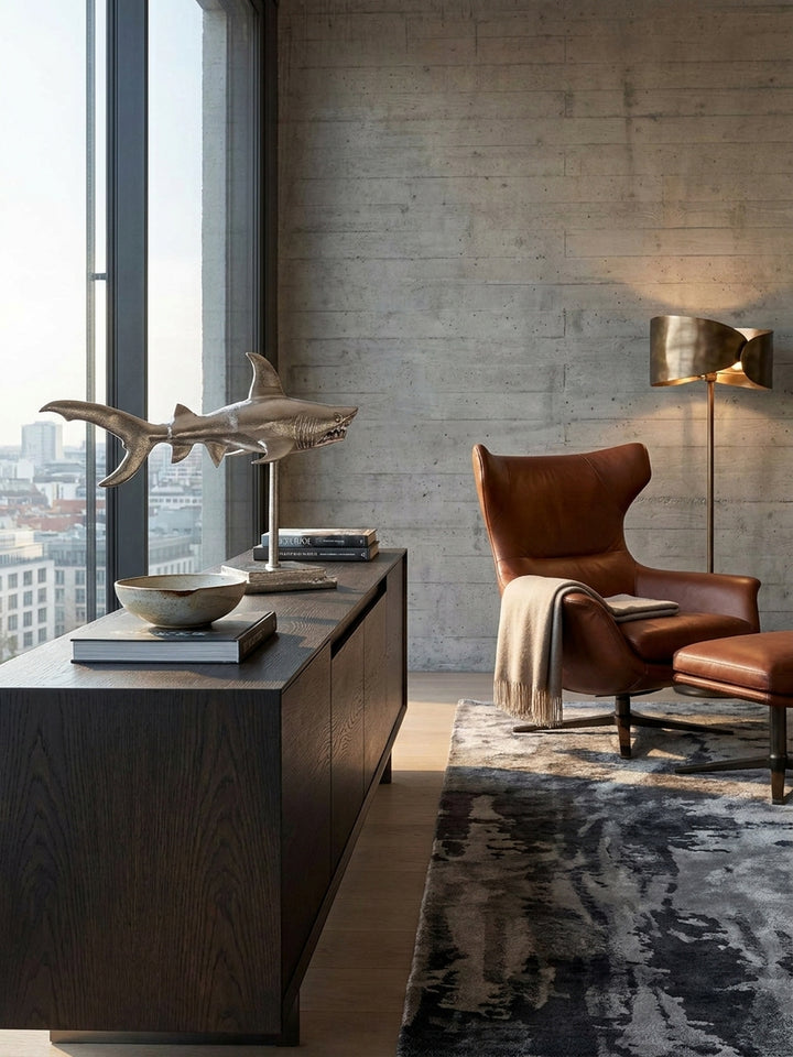 Die silberne Hai-Figur als Statement-Deko kombiniert mit einer minimalistischen Tischleuchte und einem dunklen Holzelement für ein maritimes Luxus-Ambiente._