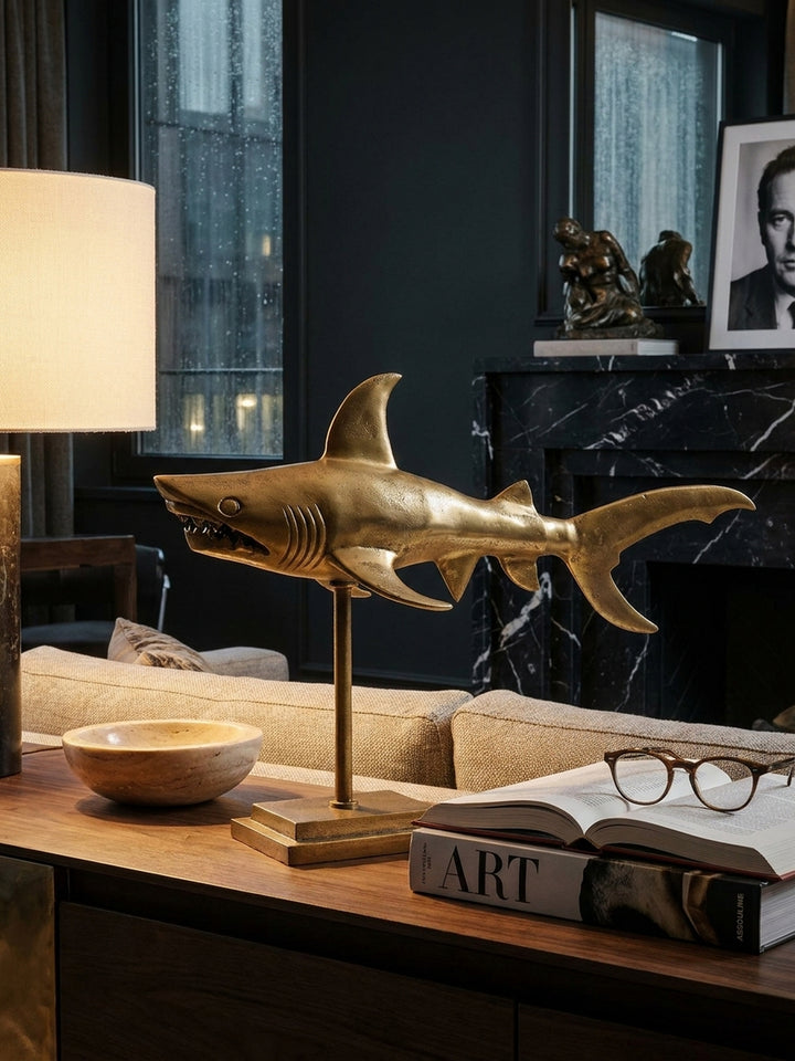 Einrichtungsdetail mit der goldenen Haifigur auf einem Regal, daneben eine minimalistische Vase und ein Stapel Bücher, die eine elegante, maritime Atmosphäre schaffen._