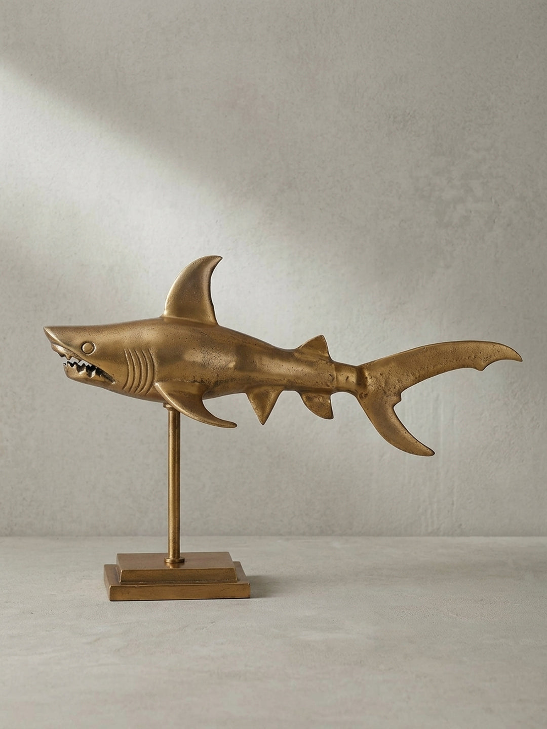Freigestellte Seitenansicht der modernen Dekofigur Hai in Gold, die ihre schlanke, 70 cm lange Silhouette und den stabilen Sockel vor weißem Hintergrund zeigt._