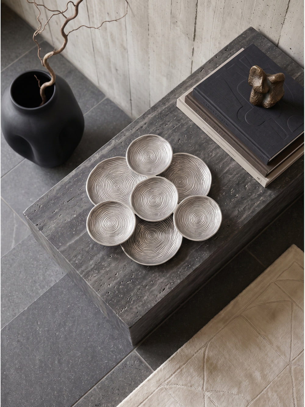 Große silberne Dekoschale aus Aluminium von oben gesehen auf einem dunklen Sideboard arrangiert mit minimalistischer Dekoration._