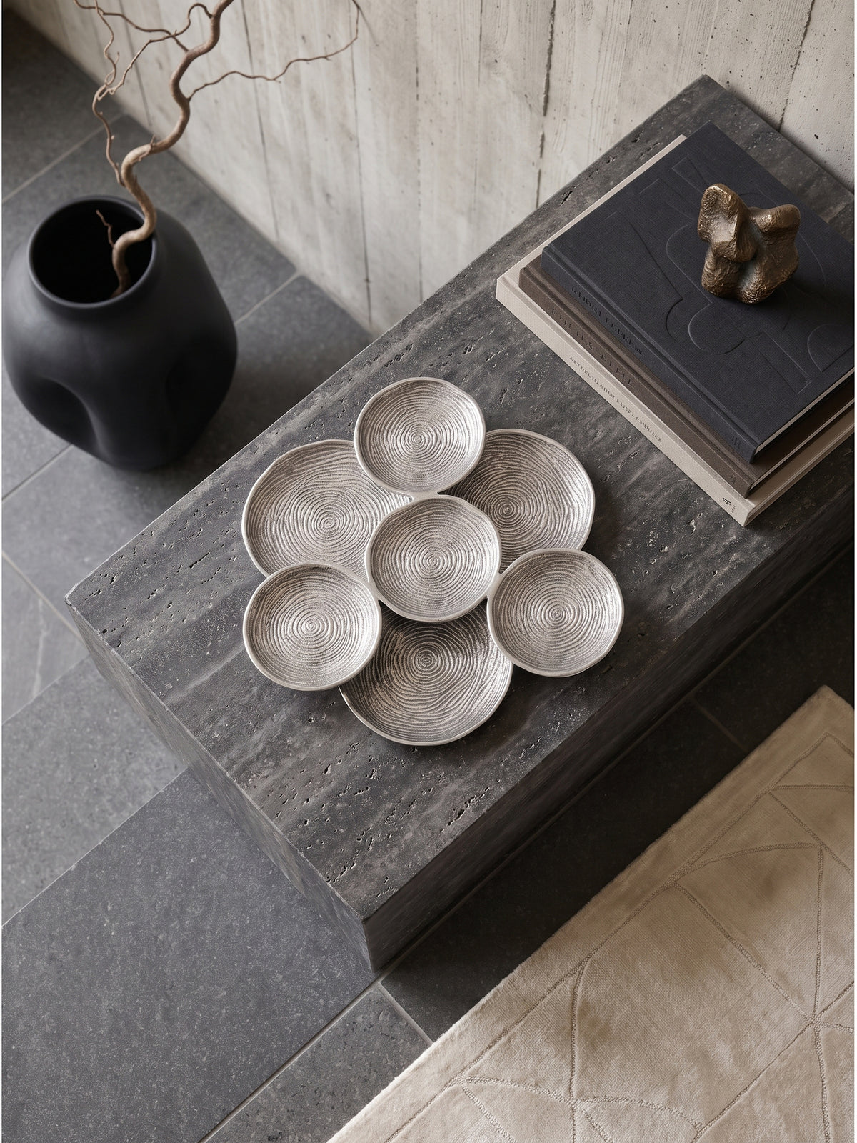 Große silberne Dekoschale aus Aluminium von oben gesehen auf einem dunklen Sideboard arrangiert mit minimalistischer Dekoration._