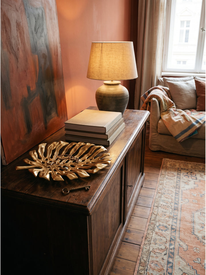 Elegante Flurgestaltung mit der goldenen Dekoschale auf einem Nussbaum-Sideboard im warmen Licht einer Keramik-Tischlampe_
