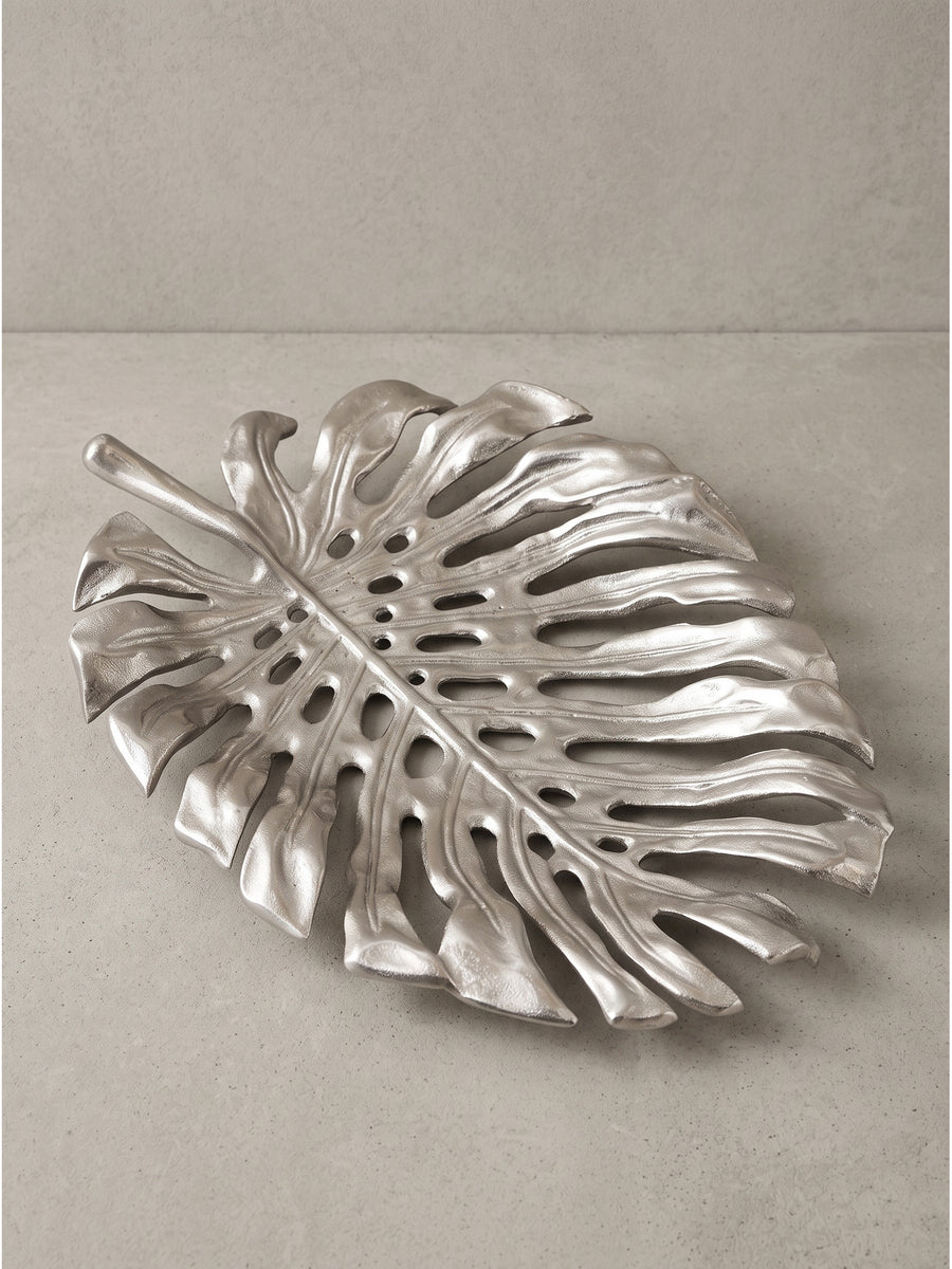 Schmuckteller aus Aluminium in Monstera-Blattform frontal freigestellt vor neutralem Hintergrund._
