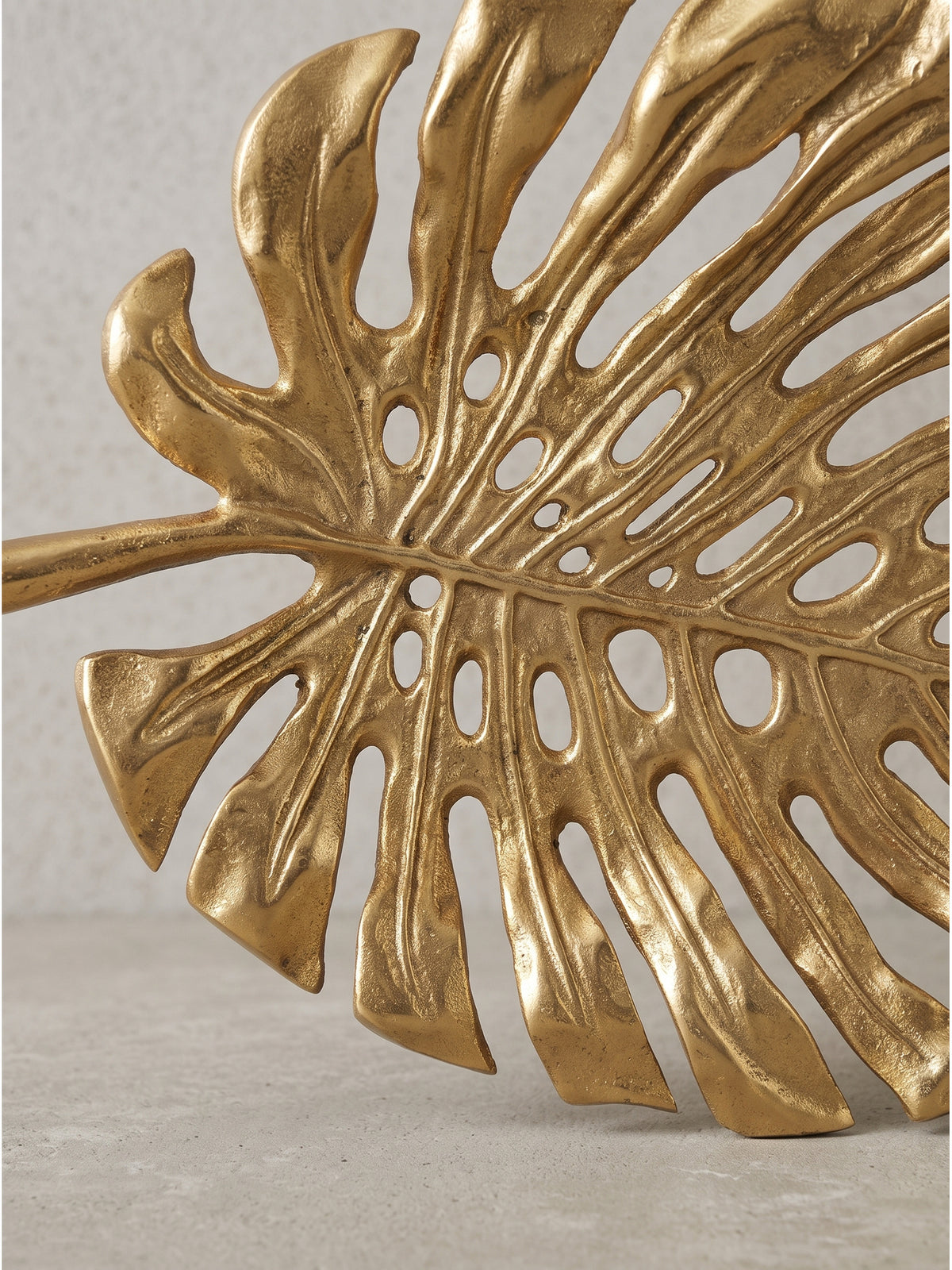 Extravagante Tischdekoration in Form eines Monstera-Blattes aus Aluminium in Gold auf neutralem Fotohintergrund_
