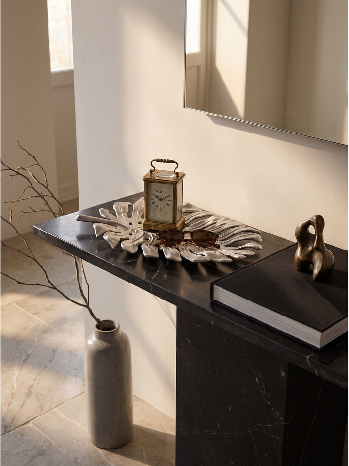 Silberne Blattschale als praktische Ablage mit Sonnenbrille und Ringen auf einem modernen Flurmöbel vor glatter weißer Wand._