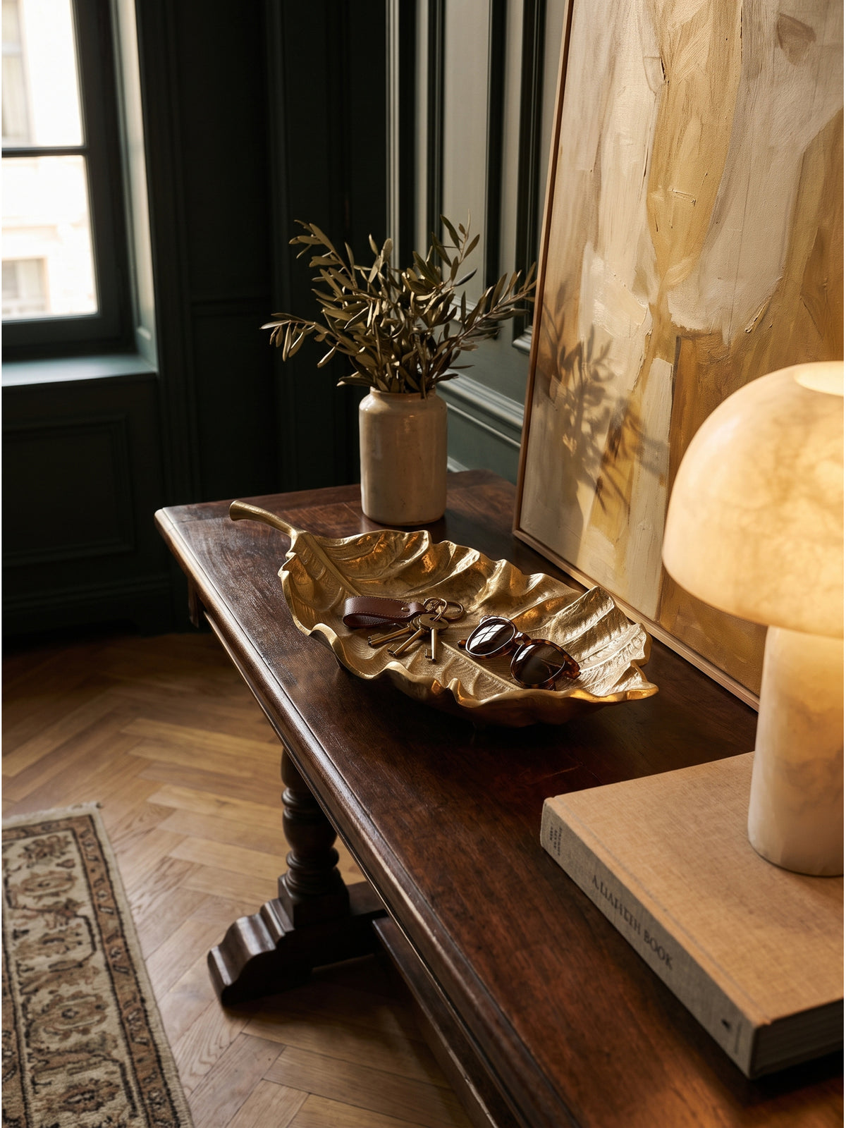 Elegantes Arrangement mit goldener Aluminiumschale, Vintage-Schlüsseln und Sonnenbrille neben einer schweren Steinlampe._