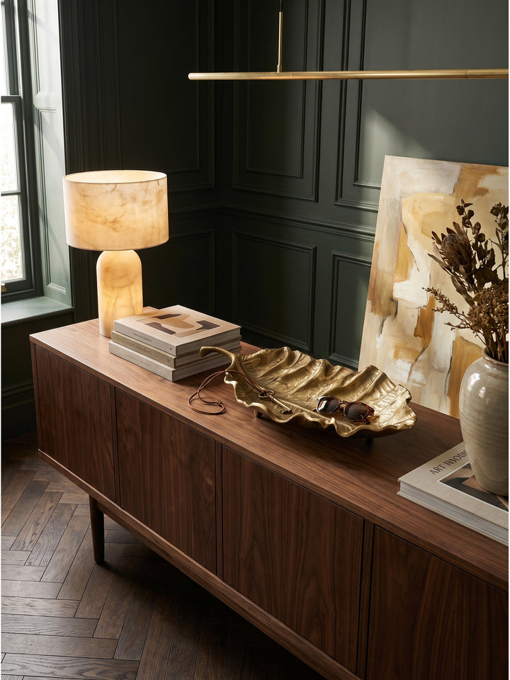 Die längliche Deko-Blattschale harmoniert perfekt mit dem warmen Holz des Sideboards und der grünen Wandtäfelung im Hintergrund._