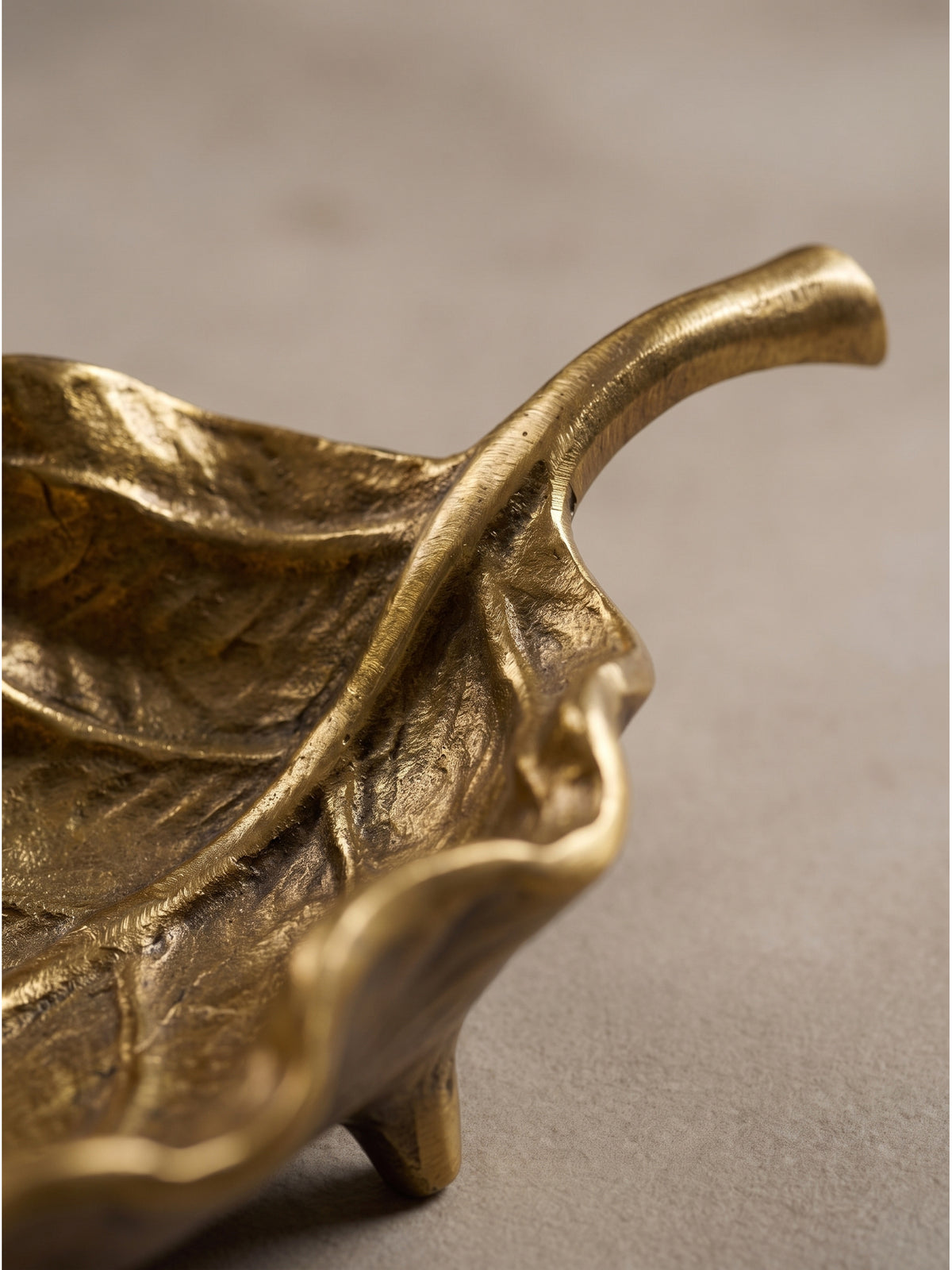 Nahaufnahme der handgefertigten gewellten Oberfläche und der filigranen Blattadern der goldenen Metallschale._