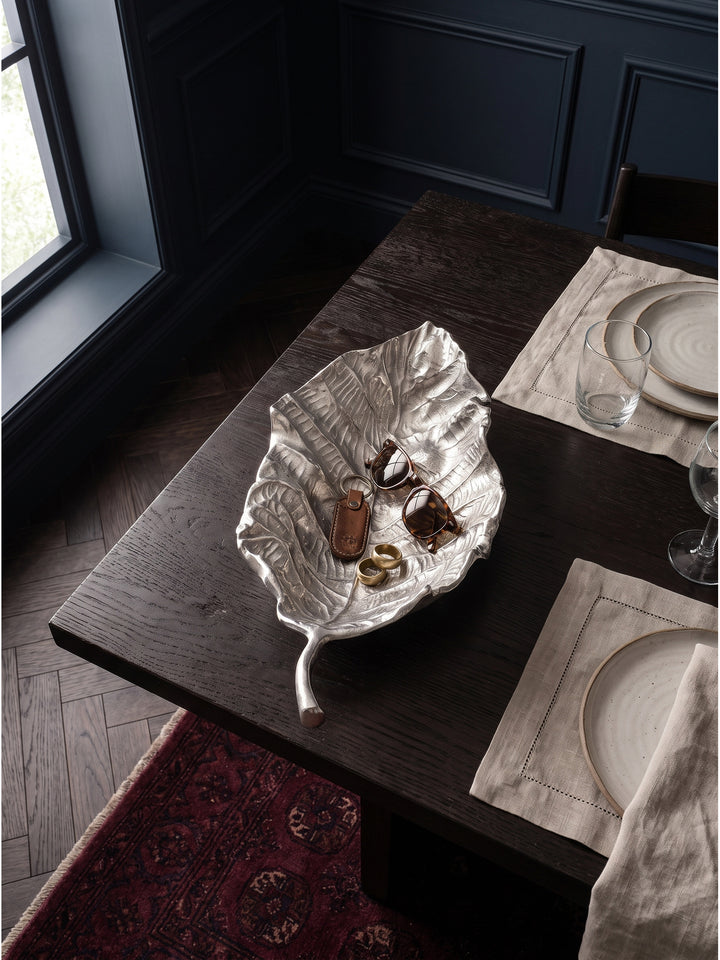 Große silberne Dekoschale in Blattform auf einer Massivholz-Konsole platziert im dunklen Eingangsbereich mit indirekter Beleuchtung_