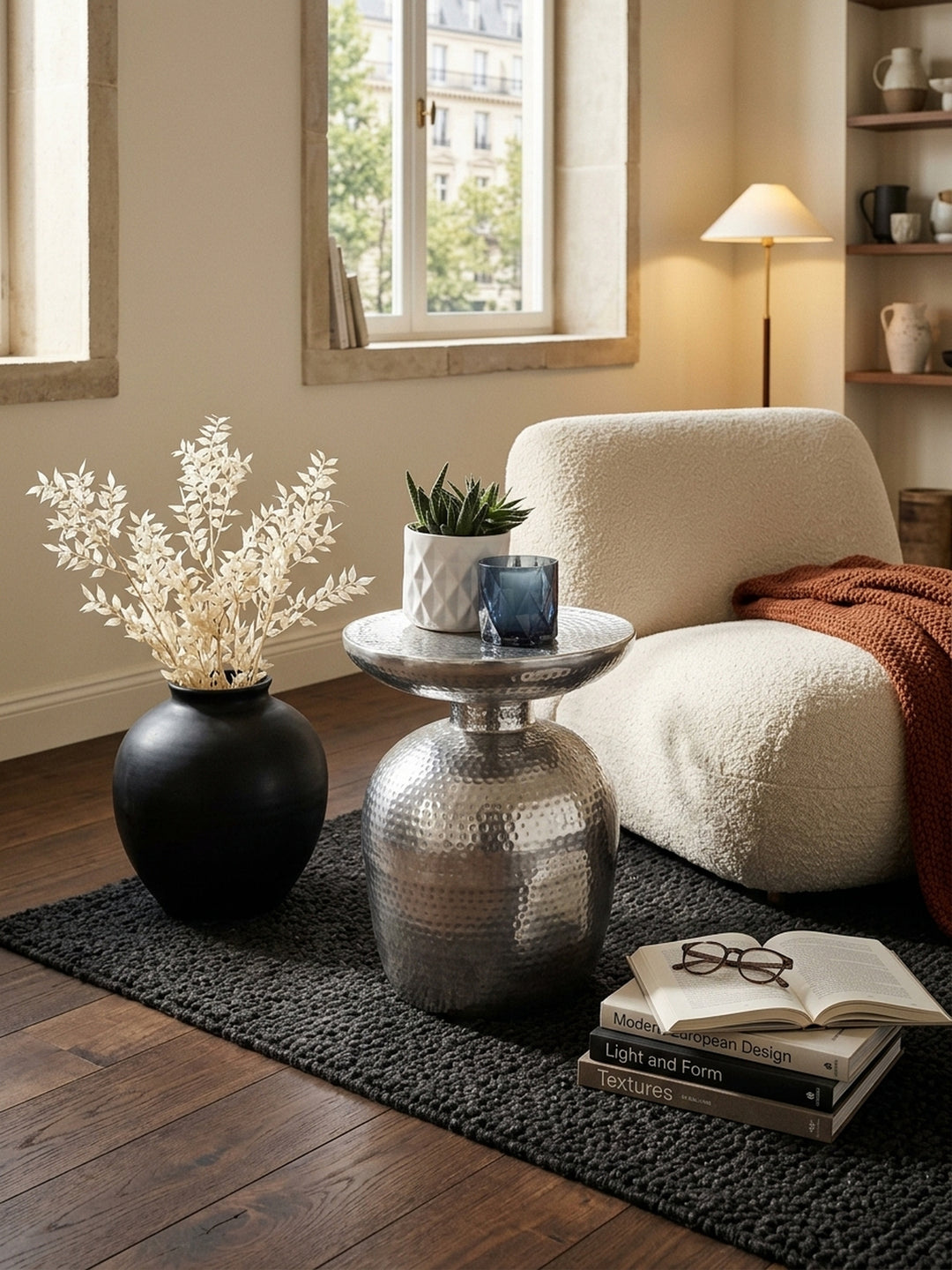 Draufsicht auf den runden silbernen Anstelltisch im Lounge-Bereich. Die 36,5cm breite Ablagefläche des Designer-Tisches aus Metall reflektiert das Licht neben dunklen Walnuss-Dielen._