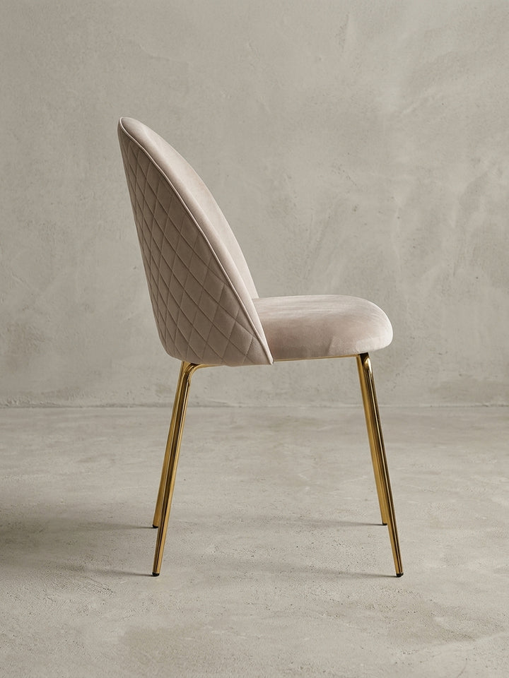 Gepolsterter Samt-Stuhl in Beige in einer dynamischen Perspektive, die das Zusammenspiel von weichem Stoff und glänzendem Metall betont._