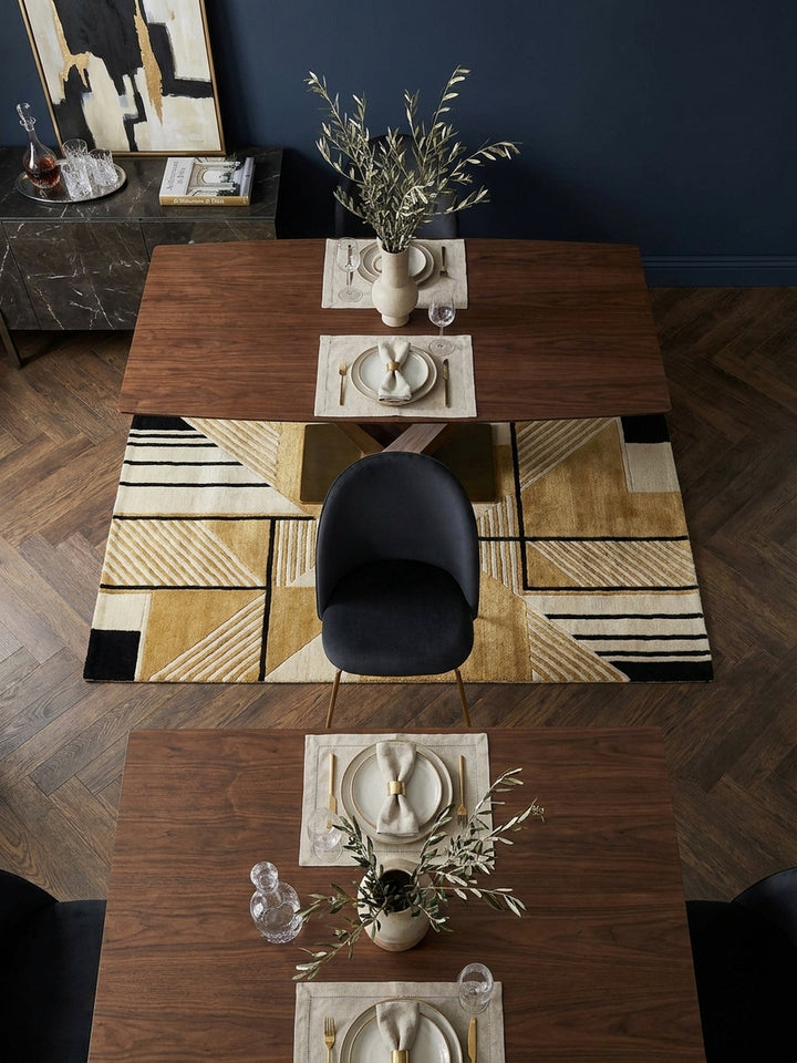 Blick von oben auf zwei schwarze Samt-Esszimmerstühle mit Rautensteppung und goldenem Gestell um einen runden Marmortisch auf einem cremefarbenen Teppich_