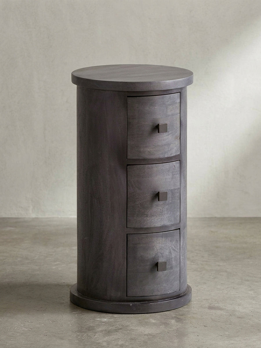 Frontansicht des zylinderförmigen Beistellschranks mit drei Schubladen aus massivem, schwarz lackiertem Mangoholz, freigestellt vor weißem Hintergrund._