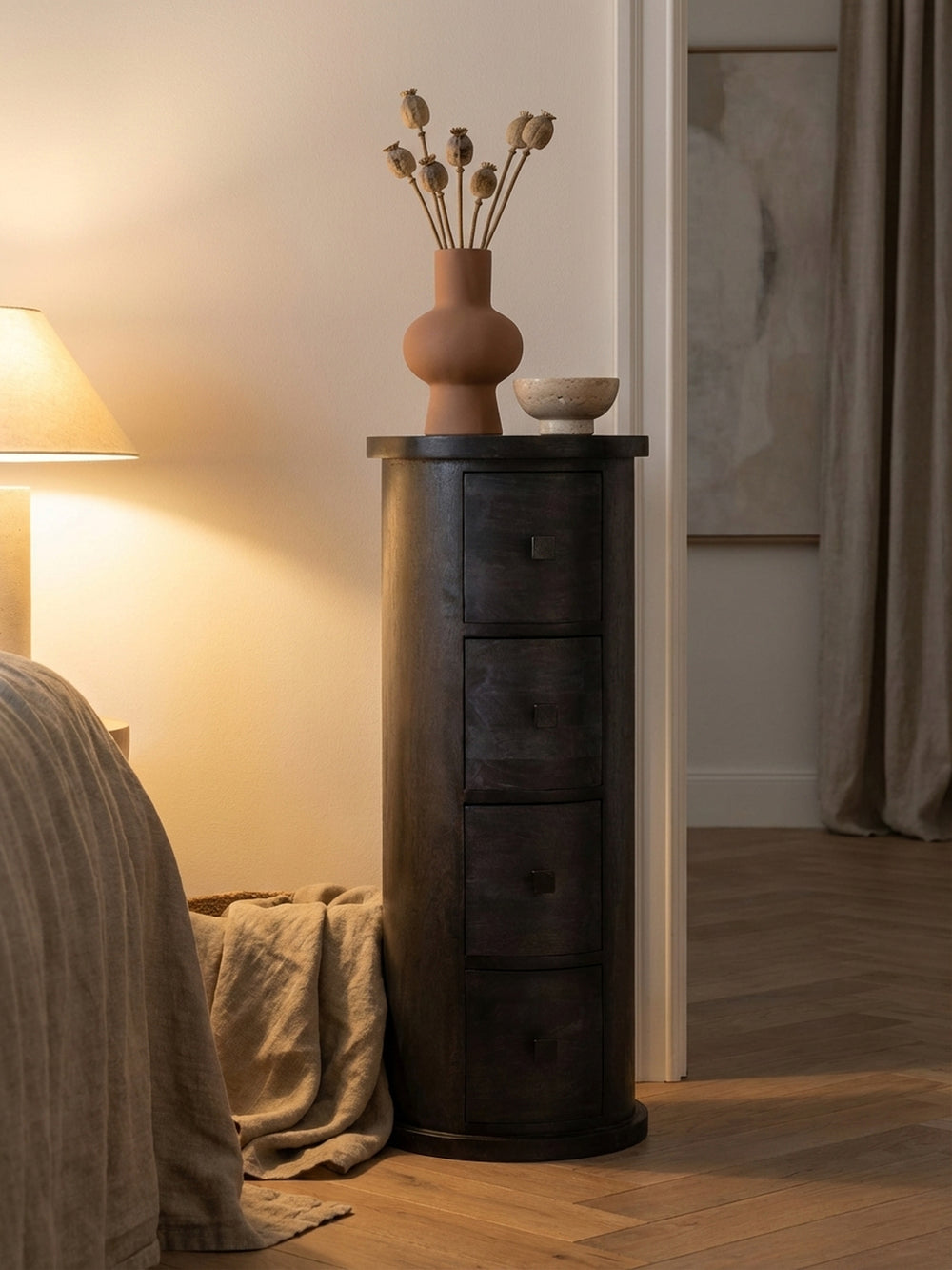 Dekoratives Arrangement auf dem schwarzen Sideboard: eine geriffelte Vase und eine Glasschale auf der runden Ablagefläche des handgefertigten Massivholzschranks._