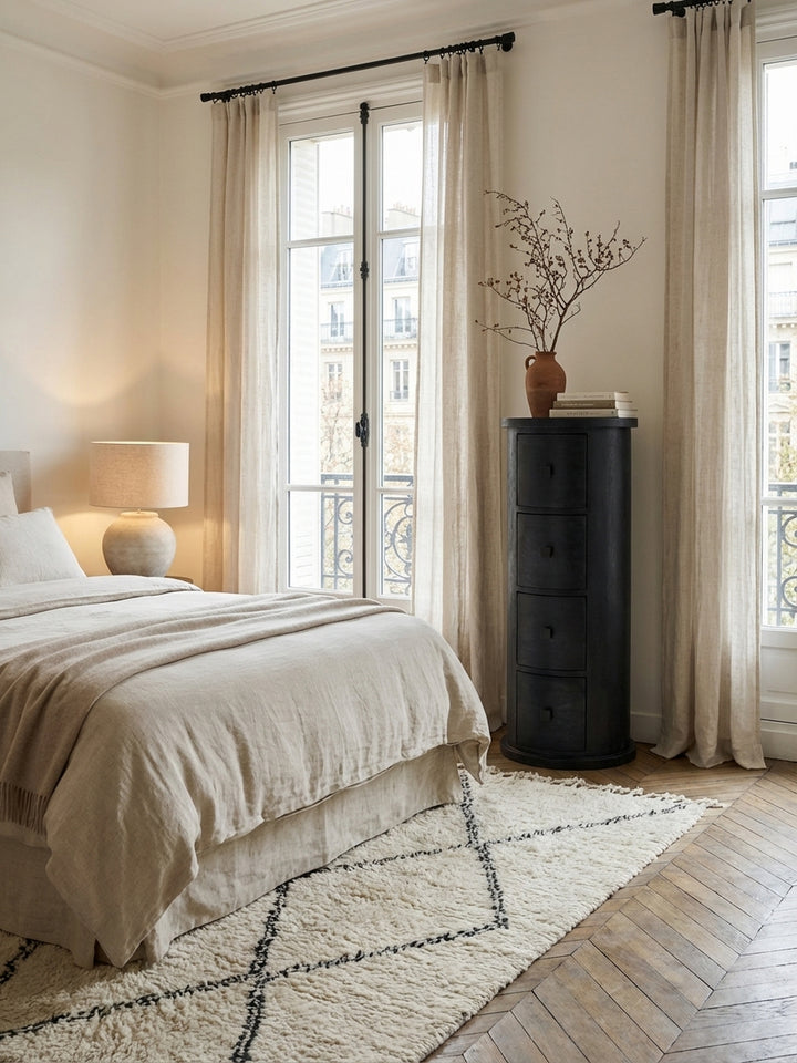 Die schmale schwarze Kommode aus Mangoholz als eleganter Nachttisch-Ersatz neben einem modernen Bett, der schmalen Stauraum im Schlafzimmer bietet._