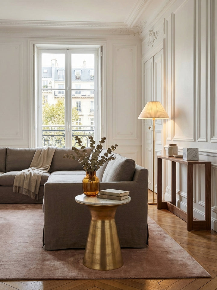 Eleganter Beistelltisch mit weißer Marmorplatte und goldenem Metallfuß neben einem Sofa in einem hellen, modernen Wohnzimmer, stilvoll dekoriert mit Vase und Tasse._