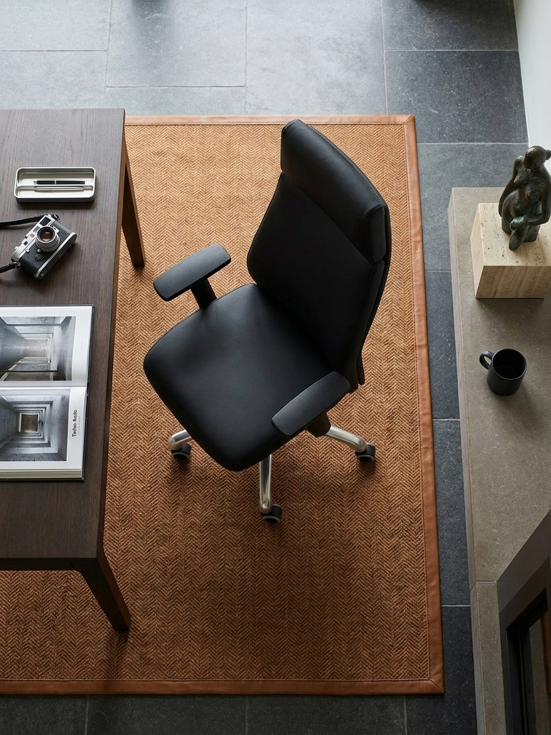 Draufsicht auf den massiven schwarzen Leder-Bürostuhl mit poliertem Aluminium-Fußkreuz, freistehend im eleganten, lichtdurchfluteten Arbeitszimmer._